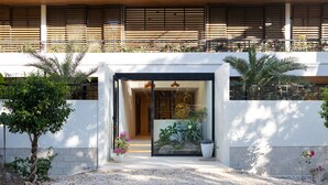 A modern building entrance with a gravel driveway, potted plants, and a wooden slatted wall above. - Silvestre Nosara, Hotel & Residences (Nosara)