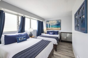A hotel room with two beds, a view of the sea, and a painting of a beach scene.