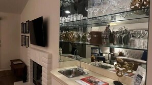 A modern kitchen with a built-in TV, a fireplace, and a glass display of wine glasses and bottles.
