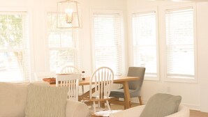 A bright dining area with a wooden table, white chairs, and a chandelier.