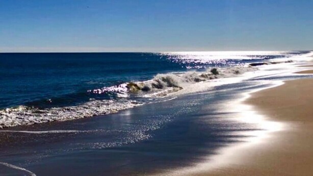 A beach with waves crashing onto the shore and a clear sky.