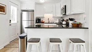 A modern kitchen with white cabinets, a stainless steel refrigerator, a coffee maker, and two bar stools.