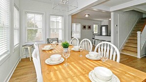 A dining area with a wooden table set for six, white chairs, and a hanging light fixture.