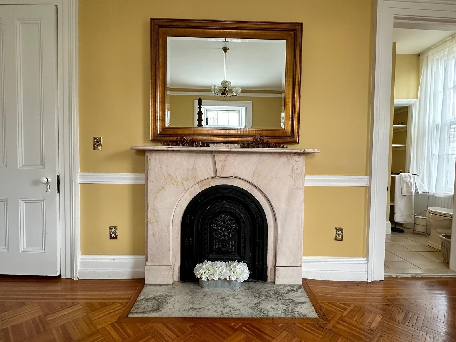 A room with a fireplace, a mirror above it, and a door to the left.