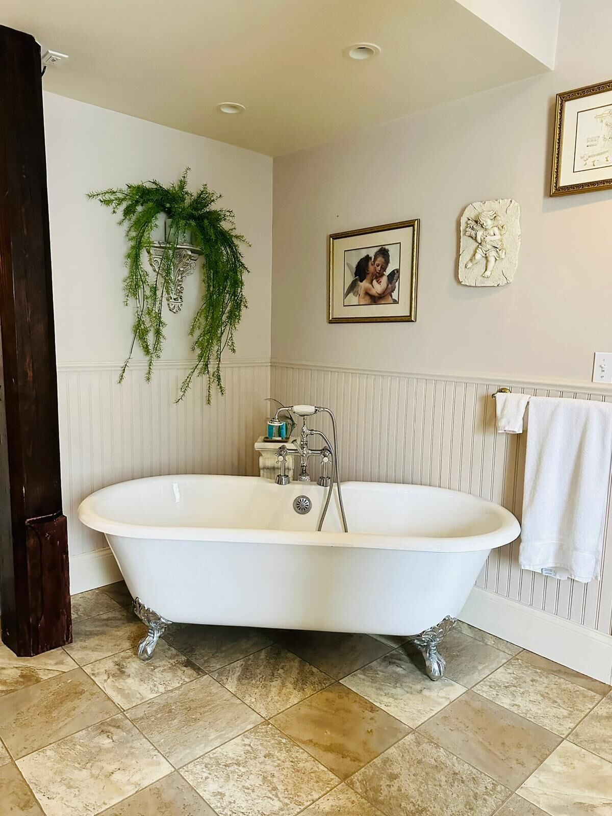 A bathroom with a freestanding clawfoot bathtub, a potted plant, a framed picture, and a towel rack.