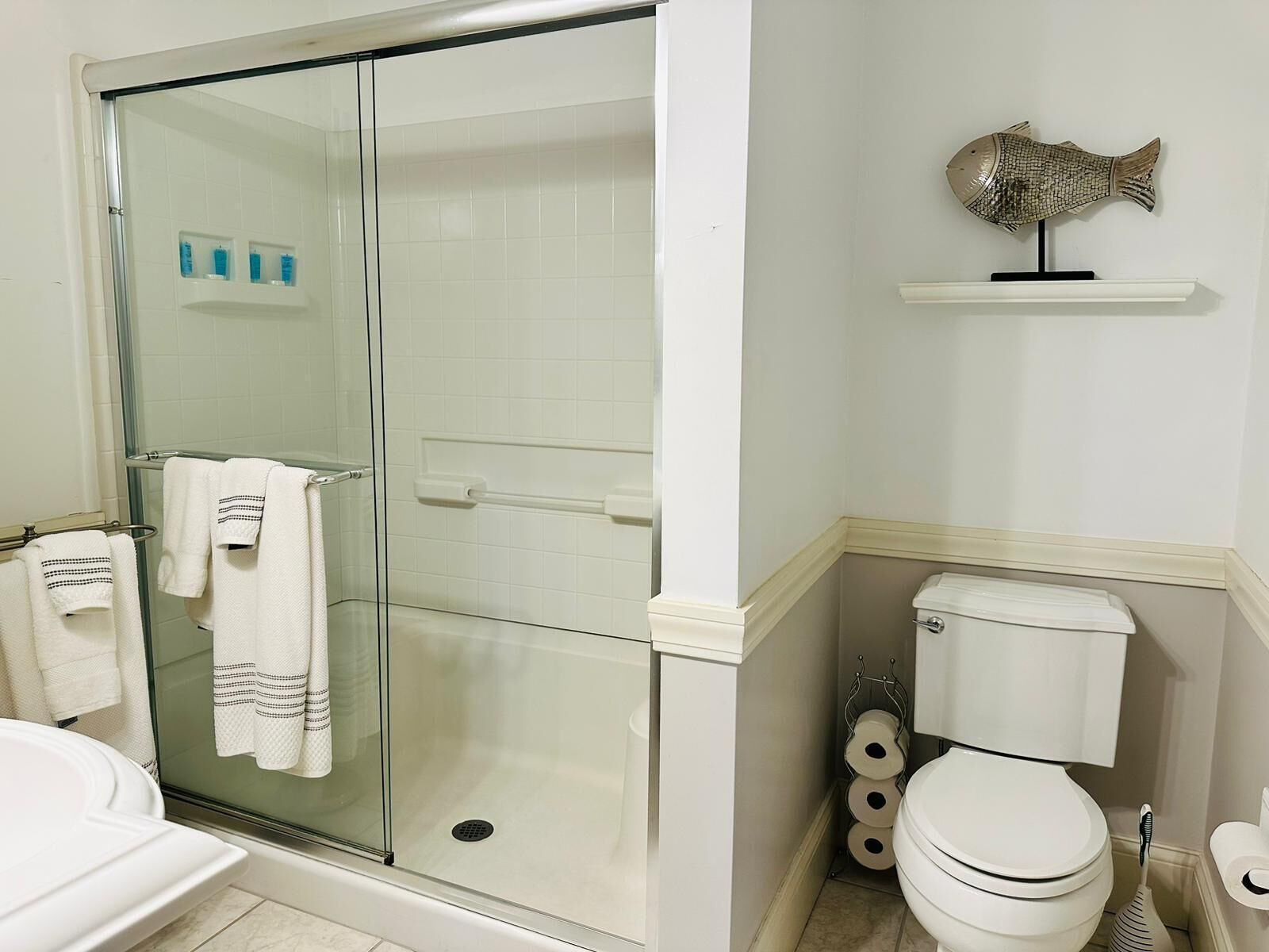 Une salle de bain avec une douche à parois de verre, des toilettes et une étagère contenant des articles de toilette.