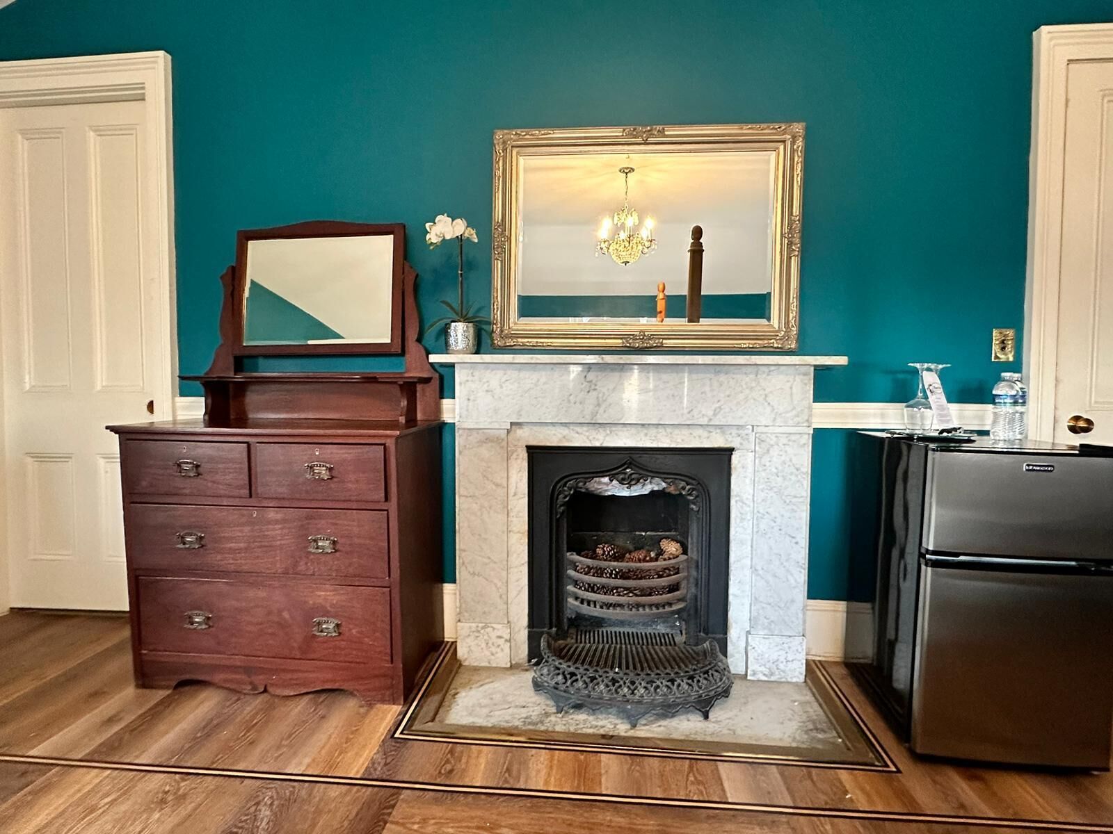 A kitchen with teal walls, a wooden dresser, a marble fireplace, and a stainless steel refrigerator.