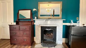 A kitchen with teal walls, a wooden dresser, a marble fireplace, and a stainless steel refrigerator.
