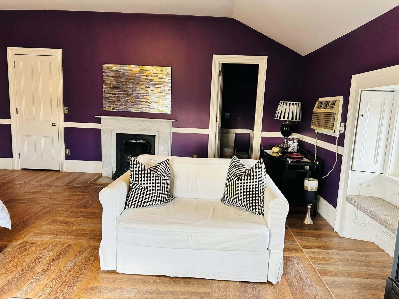 A living room with a white sofa, houndstooth pillows, a fireplace, and a modern abstract painting.