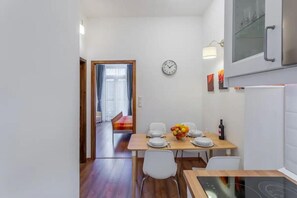 A modern kitchen with a dining area, a clock on the wall, and a view into another room.