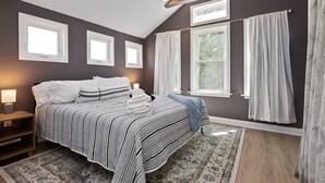 A bedroom with a large bed, a nightstand, a lamp, and a window with curtains. - Walkable Coffee, Restaurants, Shops, and Grocery! Huge backyard. (Columbus)