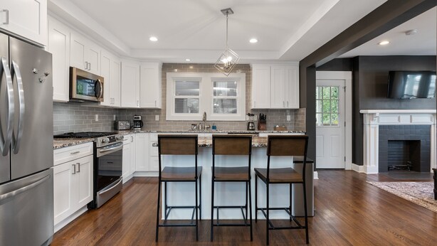 A modern kitchen with white cabinets, stainless steel appliances, a central island with bar stools, and a fireplace. - Walkable Coffee, Restaurants, Shops, and Grocery! Huge backyard. (Columbus)