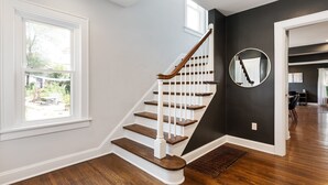 A staircase with wooden steps and white railings, leading to a dark wall with a circular mirror. - Walkable Coffee, Restaurants, Shops, and Grocery! Huge backyard. (Columbus)