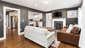 A modern living room with a sofa, a brown leather couch, and a wooden coffee table. - Walkable Coffee, Restaurants, Shops, and Grocery! Huge backyard. (Columbus)
