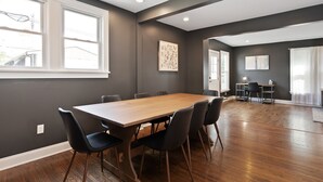 A spacious room with a large wooden table and six chairs, a dark gray wall, and a large window providing natural light. - Walkable Coffee, Restaurants, Shops, and Grocery! Huge backyard. (Columbus)