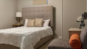 Ein Schlafzimmer mit Bett, Sessel, Deckenventilator, Nachttisch und Wandlüfter.
