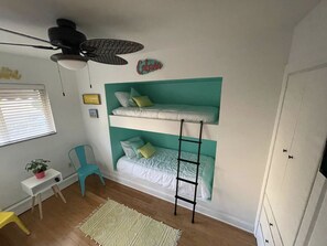 Una habitación con literas, un escritorio, una silla, una escalera y un armario.