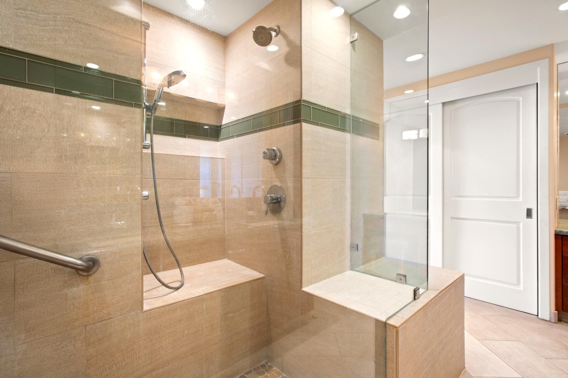A modern bathroom with a glass shower enclosure, a handrail, and a vanity with a mirror.