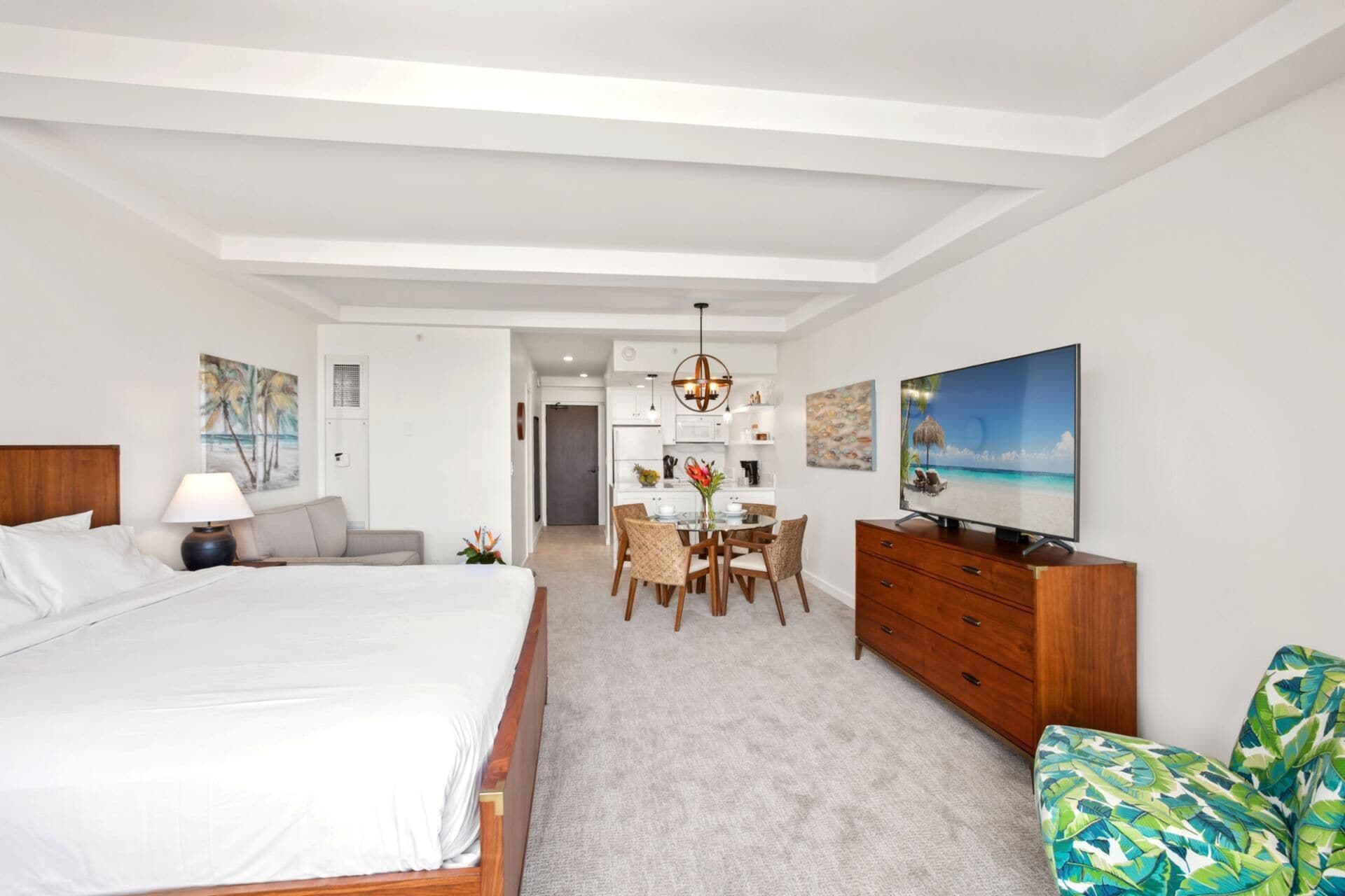 Habitación de hotel moderna con una cama grande, zona de comedor, televisor y vistas a la playa.