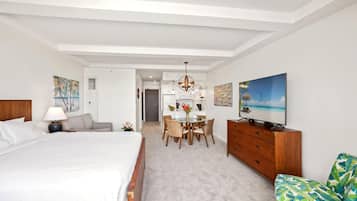 Habitación de hotel moderna con una cama grande, zona de comedor, televisor y vistas a la playa.