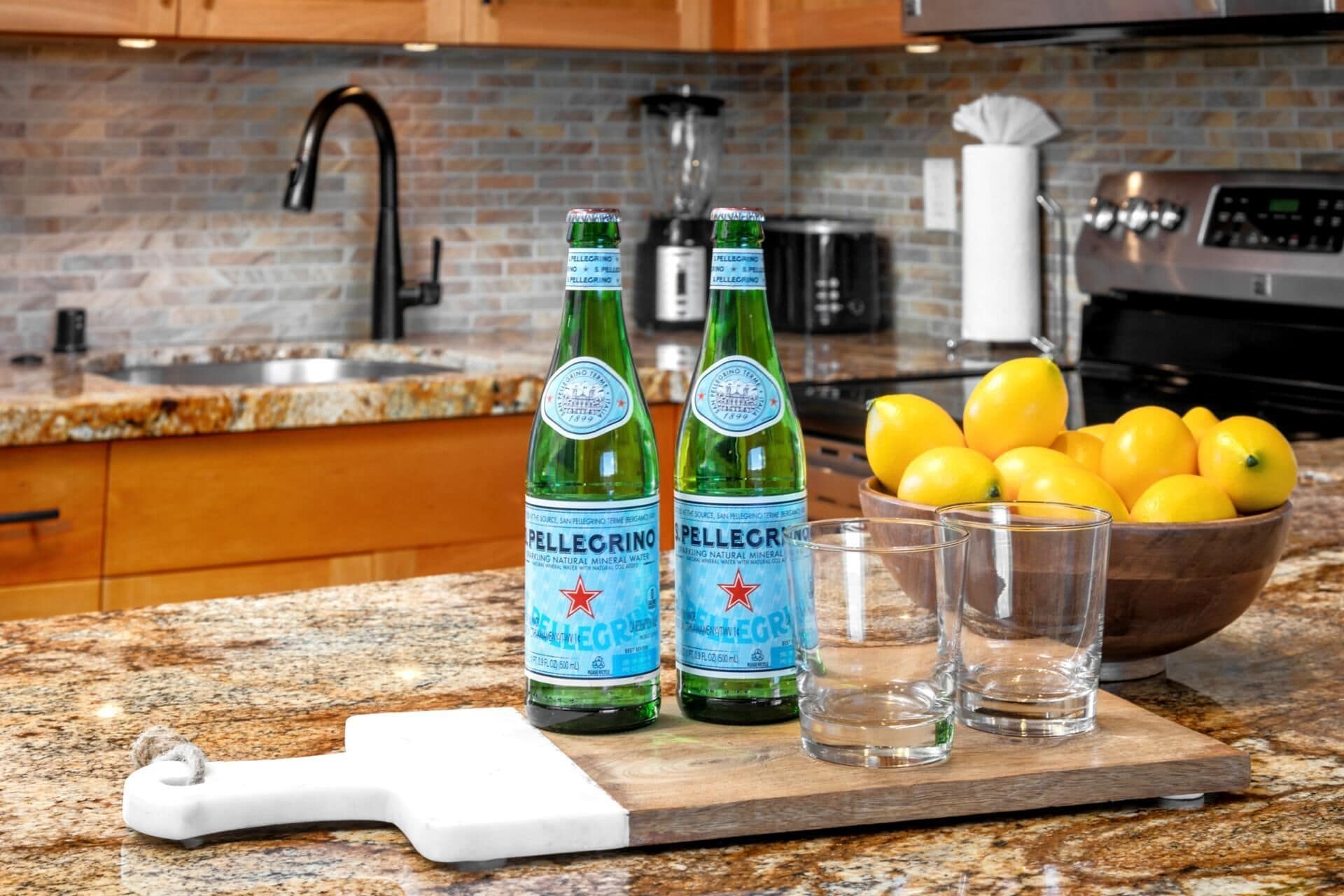 A kitchen counter with Pellegrino sparkling water bottles, a bowl of lemons, and glasses.