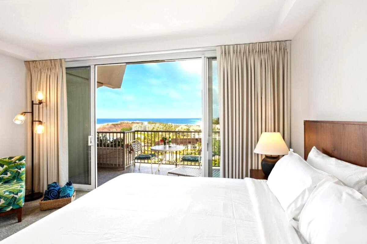 Ein Hotelzimmer mit einem Bett, einem Nachttisch, einer Lampe, einem Sessel, einem Tisch und Blick auf das Meer.