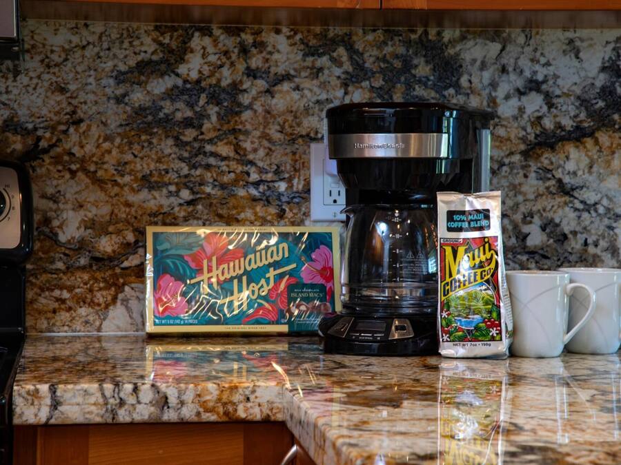 A kitchen counter with a coffee maker, a box of Hawaiian Host coffee, and a mug.