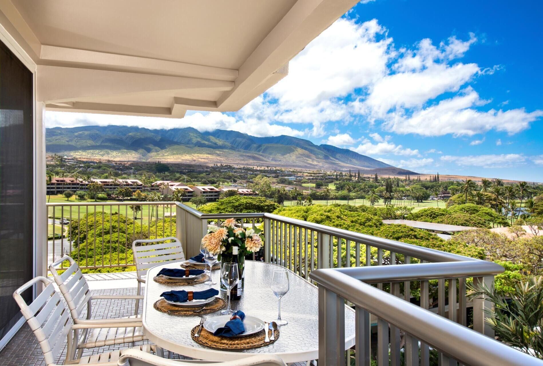 Un coin repas avec une table dressée pour quatre personnes, offrant une vue panoramique sur un paysage magnifique, avec des montagnes et une végétation luxuriante.