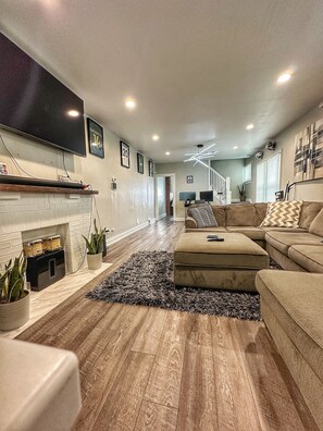 A modern living room with a fireplace, a sectional sofa, and a flat-screen TV mounted on the wall.