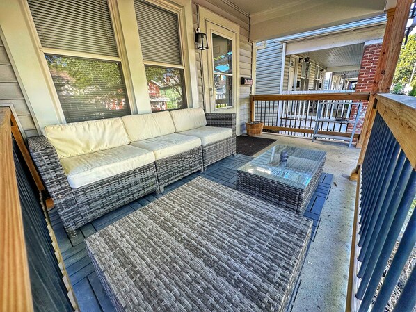 A covered porch with wicker furniture, a glass coffee table, and a view of the neighborhood.