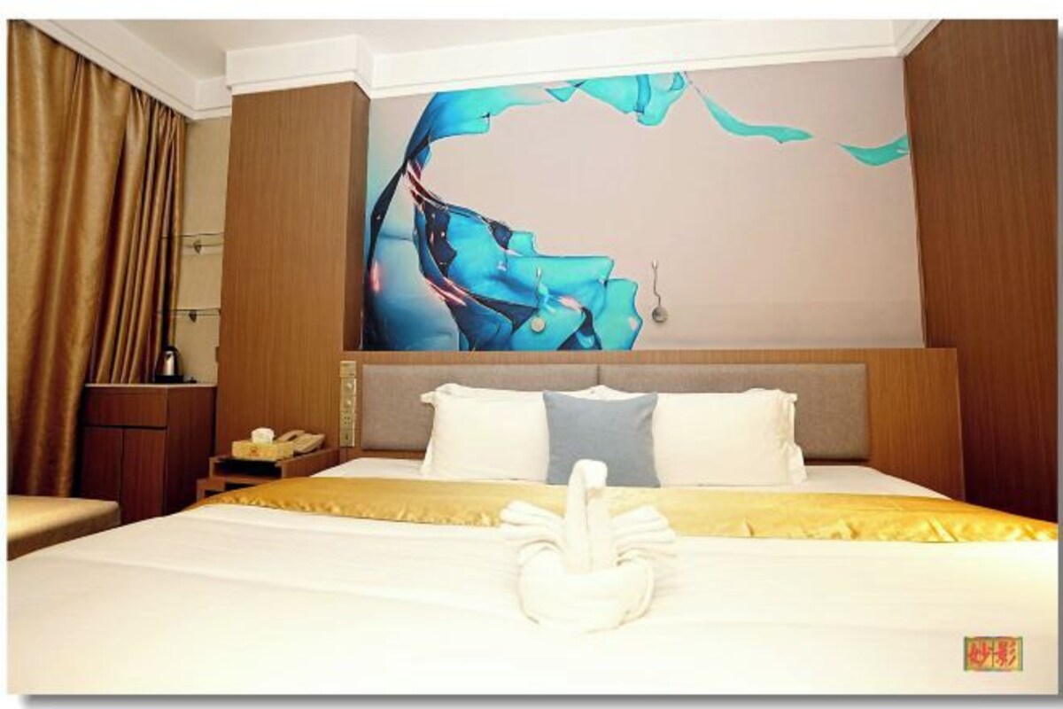 A hotel room with a bed, a wall art piece, a telephone, and a desk.