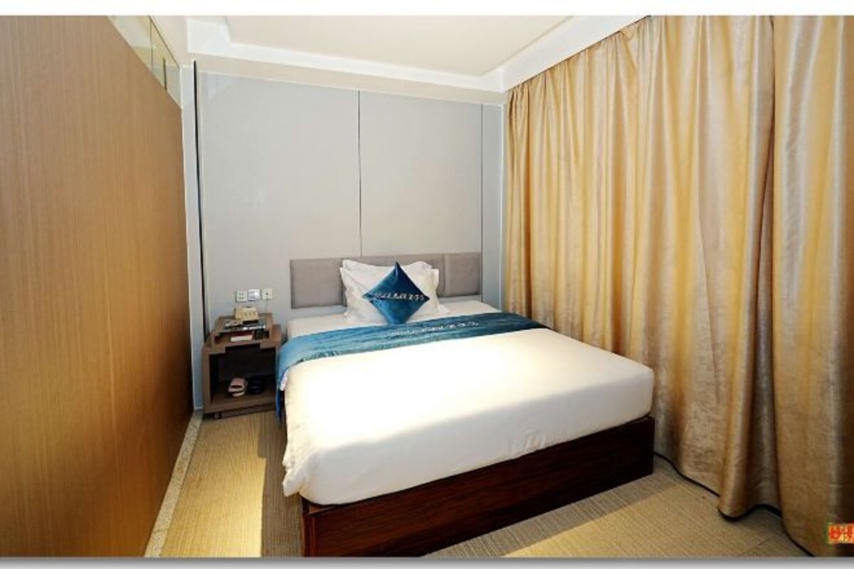 A hotel room with a bed, a nightstand, a lamp, and a curtain.