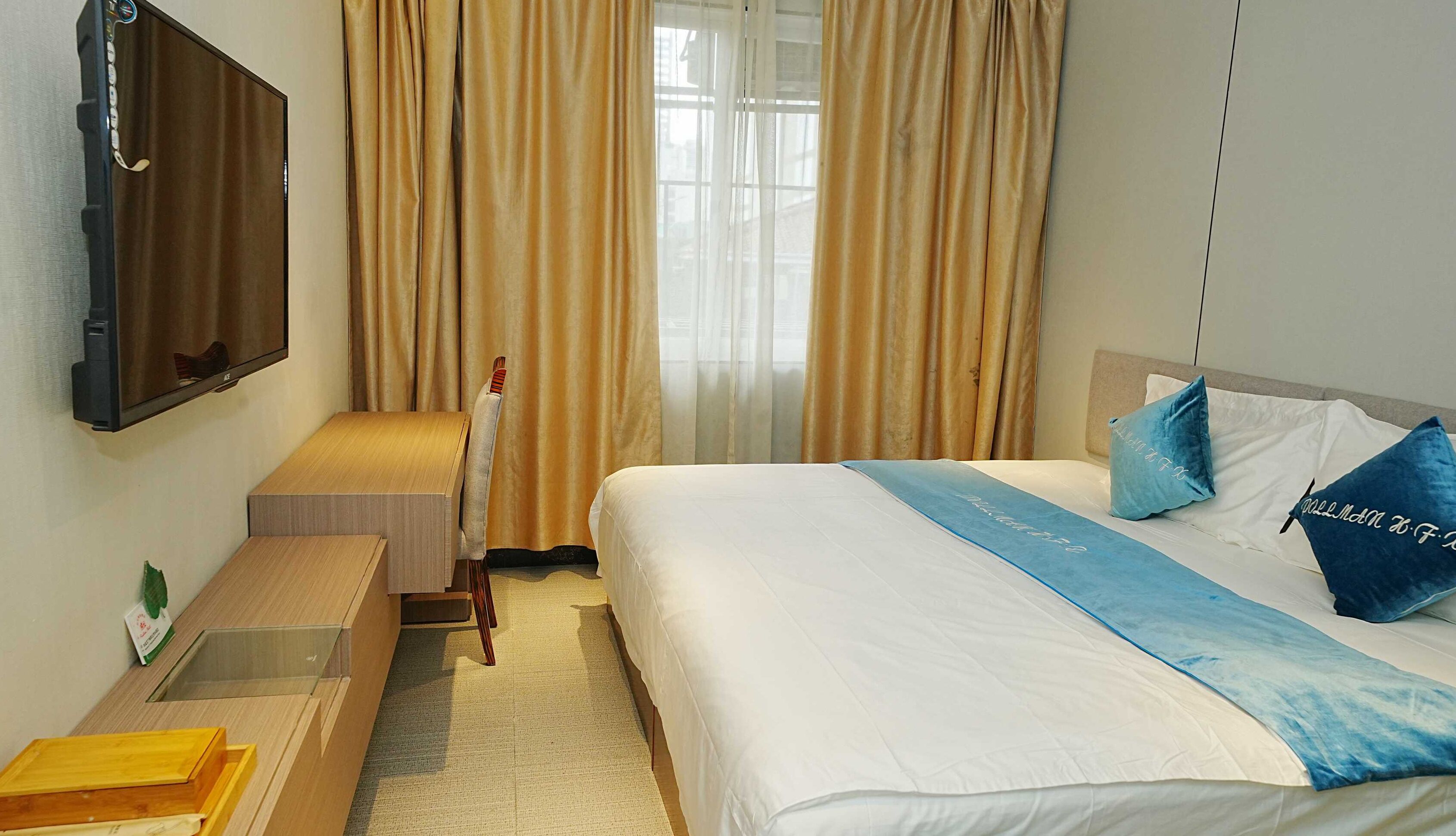 A hotel room with a bed, a desk, a chair, a television, and a window with curtains.