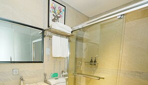 Un baño moderno con ducha envuelta en vidrio, pared con azulejos de mármol, lavabo con espejo y una obra de arte enmarcada sobre el perchero.