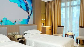 Habitación de hotel con dos camas, un escritorio con teléfono, una silla, una mesita con botellas de agua y un ventanal con cortinas.