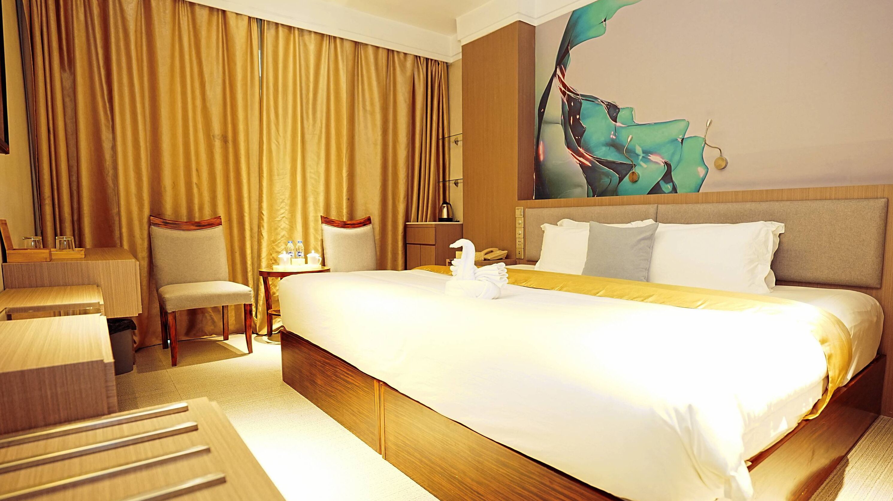 A hotel room with a large bed, a desk, a chair, and a painting on the wall.