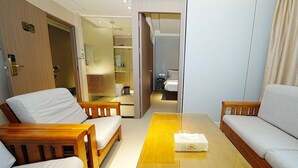 A hotel room with a wooden sofa set, a small table, and a bathroom visible through an open door. - Pristinehotel (Manila)