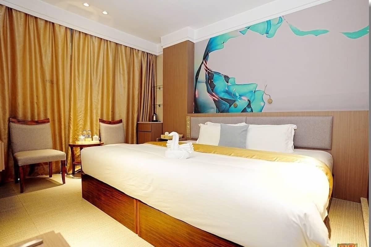 A hotel room with a large bed, a bedside table, a chair, and a wall painting.