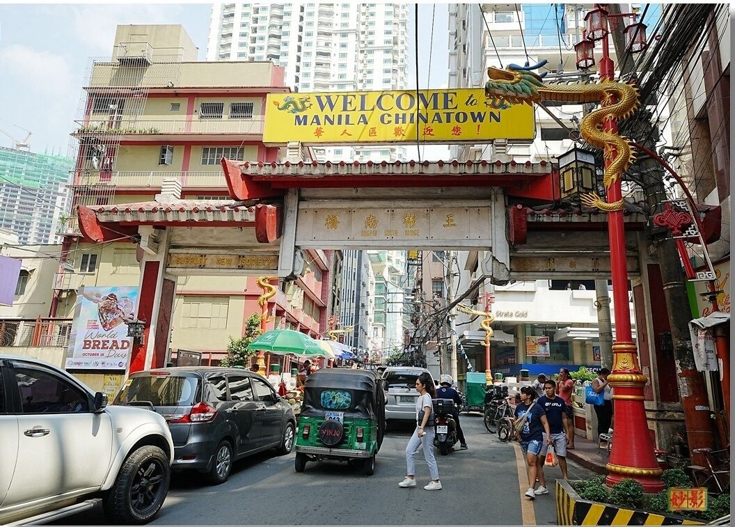 A street scene with a sign welcoming to Manila Chinatown, a red dragon decoration, and various vehicles and pedestrians.