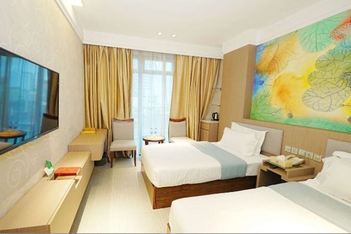 A hotel room with two beds, a TV, a desk, a chair, and a large window with curtains.