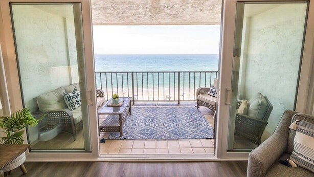 A balcony with a view of the beach, furnished with a sofa, a table, and a rug. - Respite by the Sea The Islander, King Bed, Oceanfront Condo, Pool, Tennis,Cabana (Wrightsville Beach)