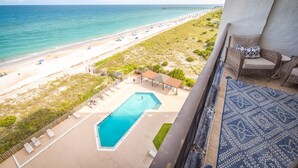A balcony with a view of a beach, a pool, and a pier in the distance. - Respite by the Sea The Islander, King Bed, Oceanfront Condo, Pool, Tennis,Cabana (Wrightsville Beach)