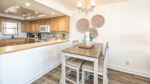 A modern kitchen with wooden cabinets, a central island, and a chandelier. - Respite by the Sea The Islander, King Bed, Oceanfront Condo, Pool, Tennis,Cabana (Wrightsville Beach)