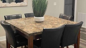 A dining area with a marble table, black chairs, a potted plant, a chandelier, and a mirror on the wall. - Grand Haven Getaway Welcomes You (Grand Haven)