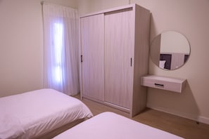 Un dormitorio con dos camas individuales, un armario, una mesita de noche y un espejo.