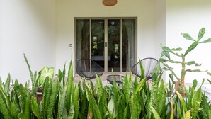 A covered patio area with two black chairs, a woven hanging light fixture, and a variety of green plants. - Arenal White Bliss Villa (La Fortuna)