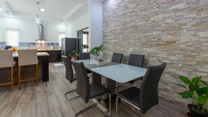A modern kitchen with a stone wall backsplash, a dining area with a glass-top table and chairs, and a visible island with a sink and countertop. - Arenal White Bliss Villa (La Fortuna)