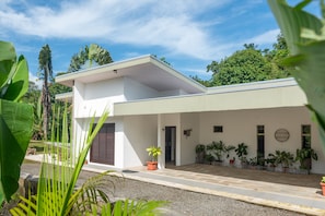 Ein modernes Haus mit flachem Dach, weißen Außenwänden und einer überdachten Veranda mit Blumentöpfen.