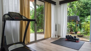 A room with a treadmill, a standing desk, and a view of a garden through large windows. - Arenal White Bliss Villa (La Fortuna)