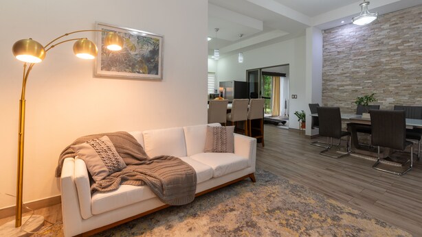 A modern living room with a white sofa, a floor lamp, and a dining area with chairs and a table. - Arenal White Bliss Villa (La Fortuna)